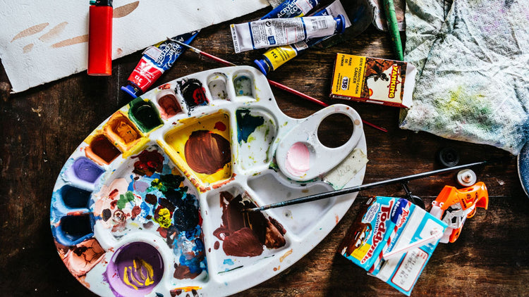 Artist's palette with mixed paint, brushes and paint tubes on a wooden worktable