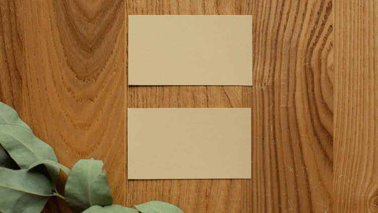 Two blank kraft paper business cards on a wooden table beside eucalyptus leaves