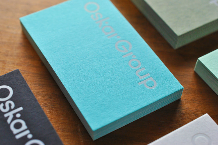 Stacks of teal, green, black and white business cards showing varied paper colours and finishes.