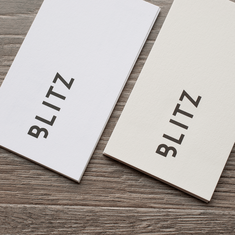 White and warm-white business card samples printed with the BLITZ wordmark on a grey wood surface.