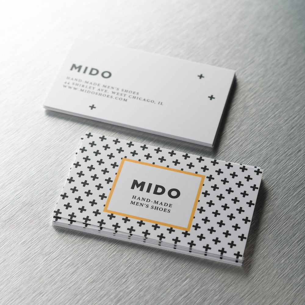 Stacks of white silk business cards with a black cross pattern and a gold-bordered logo.